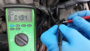 Serviser u plavim zaštitnim rukavicama priključuje pipete sa zelenog multimetra na priključcima jedne elektronske komponente u postupku ispitivanja dovoda napajanja u postupku Elektronika automobila – dijagnostika i popravka